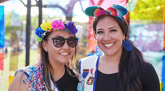 Two women dressed up in fiesta ribbons and sashes and smiling